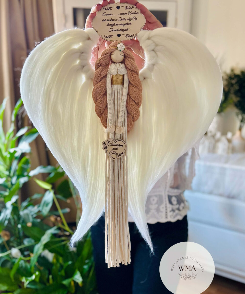Duża personalizowana dekoracja ścienna Anioł Stróż z makramy - figurka aniołka z długimi brązowymi włosami z białą różyczką i złotym paskiem w kremowej sukni z frędzli z drewnianym sercem z napisem Czuwam nad Tobą, ogromne białe skrzydła w kształcie serca, drewniana tabliczka z dedykacją, handmade