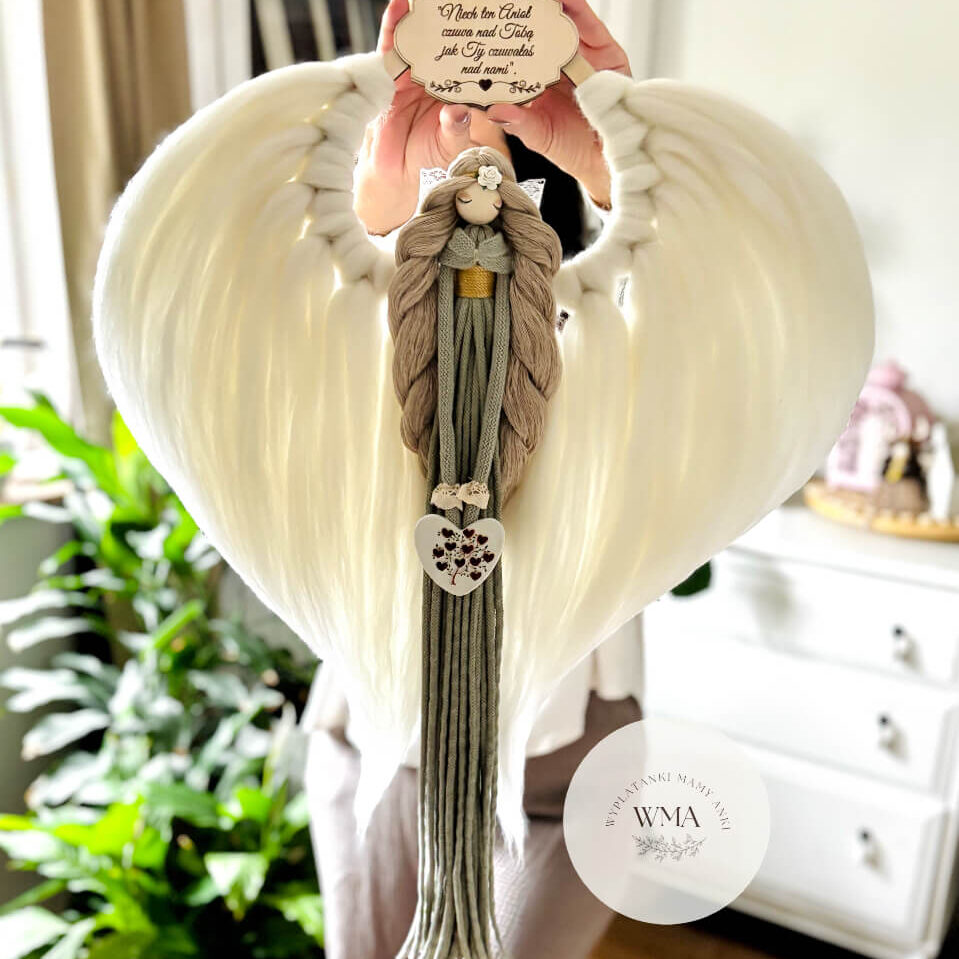 Duża personalizowana dekoracja ścienna Anioł z makramy - figurka aniołka z długimi beżowymi włosami z białą różyczką i złotym paskiem w oliwkowej sukni z frędzli z drewnianym sercem z motywem kwiatowym, ogromne białe skrzydła w kształcie serca, drewniana tabliczka z dedykacją, handmade