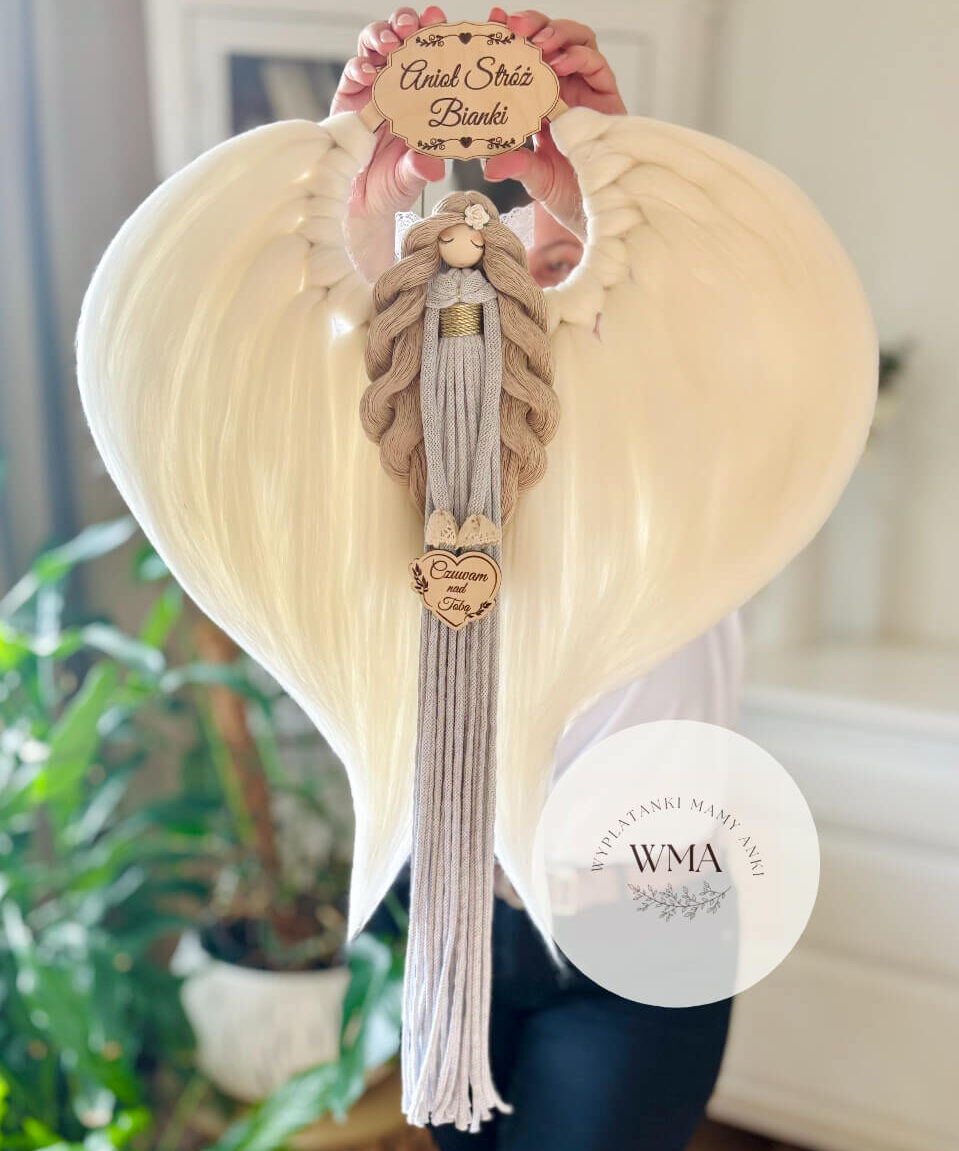 Duża personalizowana dekoracja ścienna Anioł Stróż z makramy - figurka aniołka z długimi beżowymi włosami z białą różyczką i złotym paskiem w szaro-beżowej sukni z frędzli z drewnianym sercem z napisem Czuwam nad Tobą, ogromne białe skrzydła w kształcie serca, drewniana tabliczka z imieniem, handmade