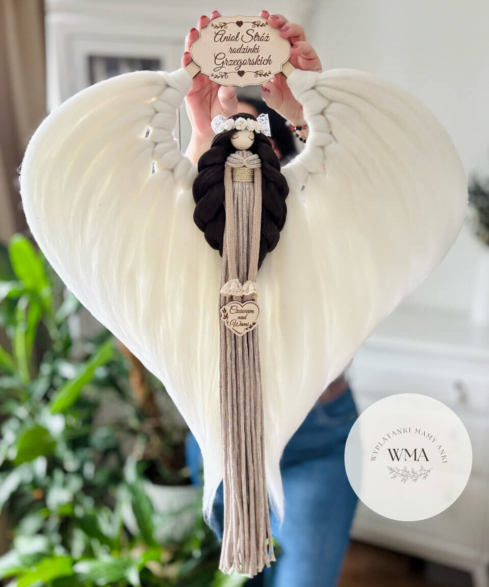 Duża personalizowana dekoracja ścienna Anioł Stróż rodziny z makramy - figurka aniołka z długimi ciemnymi włosami w białym wianku z róż i złotym paskiem w beżowo-szarej sukni z frędzli z drewnianym sercem z napisem Czuwam nad Wami, ogromne białe skrzydła w kształcie serca, drewniana tabliczka z nazwiskiem rodziny, handmade