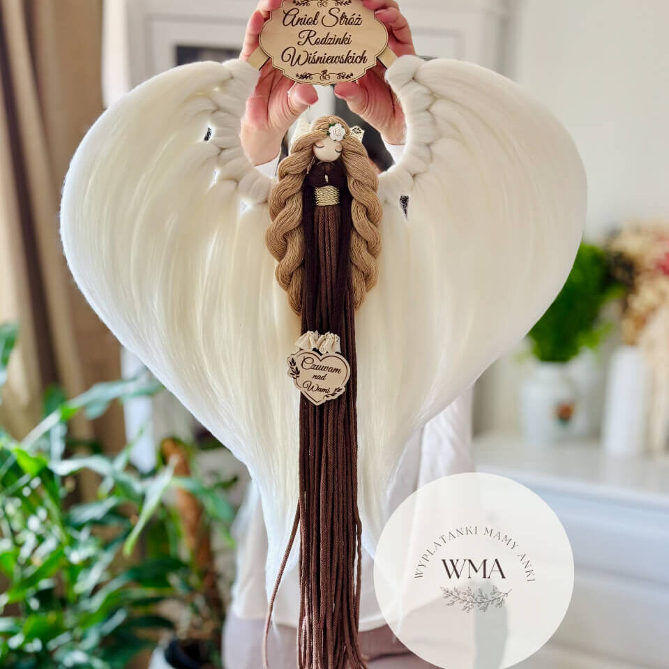 Duża personalizowana dekoracja ścienna Anioł Stróż rodziny z makramy - figurka aniołka z długimi beżowymi włosami z białą różyczką i złotym paskiem w brązowej sukni z frędzli z drewnianym sercem z napisem Czuwam nad Wami, ogromne białe skrzydła w kształcie serca, drewniana tabliczka z nazwiskiem rodziny, handmade