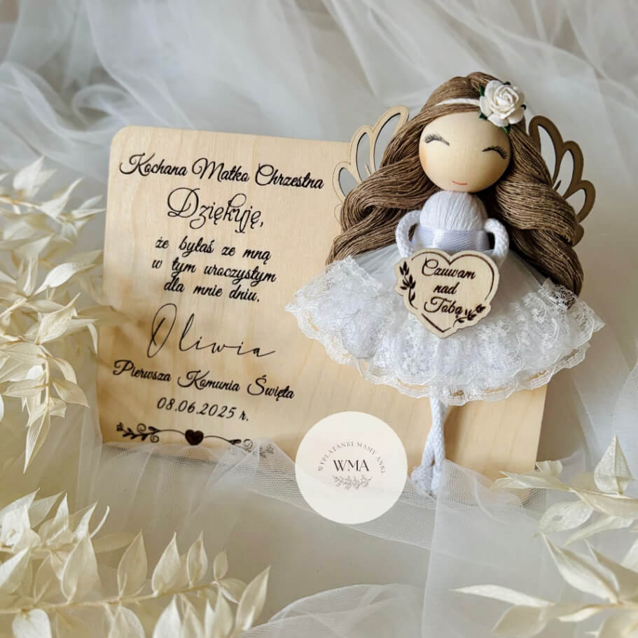 Ręcznie robiony aniołek z makramy w białej tiulowej sukience z koronką i białą różą we włosach, na drewnianej tabliczce z personalizowanym podziękowaniem dla matki chrzestnej za Pierwszą Komunię Świętą, drewniane skrzydełka, serduszko Czuwam nad Tobą
