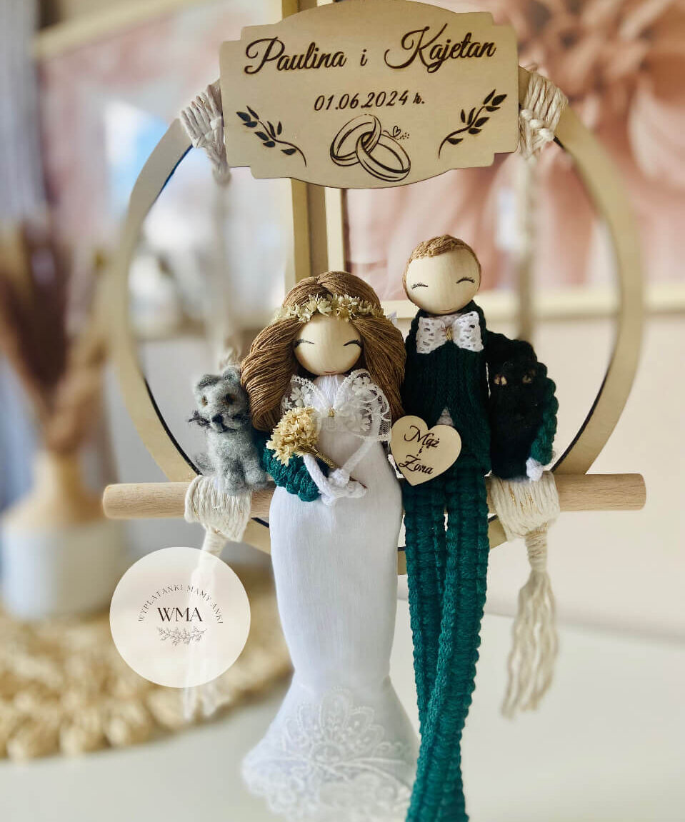 Personalizowana dekoracja ślubna na obręczy makramowej z figurkami pary młodej siedzącymi na drążku - panna młoda z brązowymi włosami w wianku i sukni koronkowej z szarym kotem, pan młody w zielonym stroju z makramy z czarnym kotem, drewniana tabliczka z imionami i datą ślubu, serce z napisem Mąż i Żona, handmade