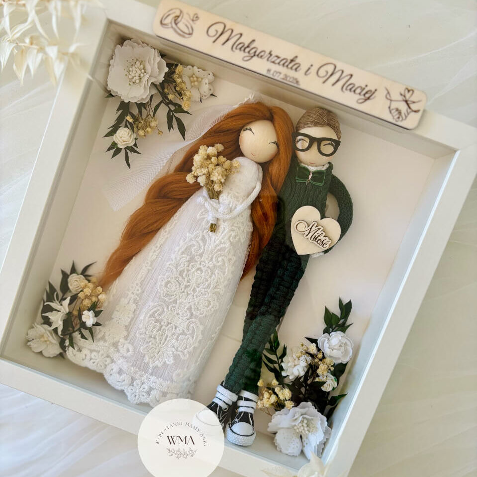 Personalizowana ramka ślubna z figurkami pary młodej - panna młoda z długimi rudymi włosami w welonie i sukni koronkowej, pan młody w zielonym swetrze z makramy w okularach i trampkach, drewniana tabliczka z imionami i datą ślubu, serce z napisem Miłość, dekoracja z białych kwiatów i suszonych traw, handmade