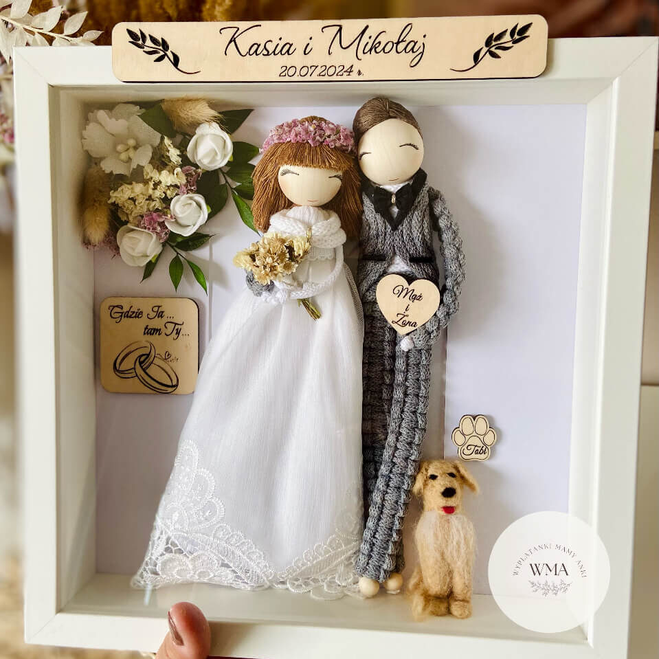 Personalizowana ramka ślubna z figurkami pary młodej i miniaturą psa - panna młoda z rudymi włosami w sukni koronkowej, pan młody w szarym stroju z makramy, filcowy pies z tabliczką z imieniem, drewniane akcesoria z napisami Mąż i Żona oraz Gdzie Ja tam Ty, dekoracja z suszonych kwiatów, handmade