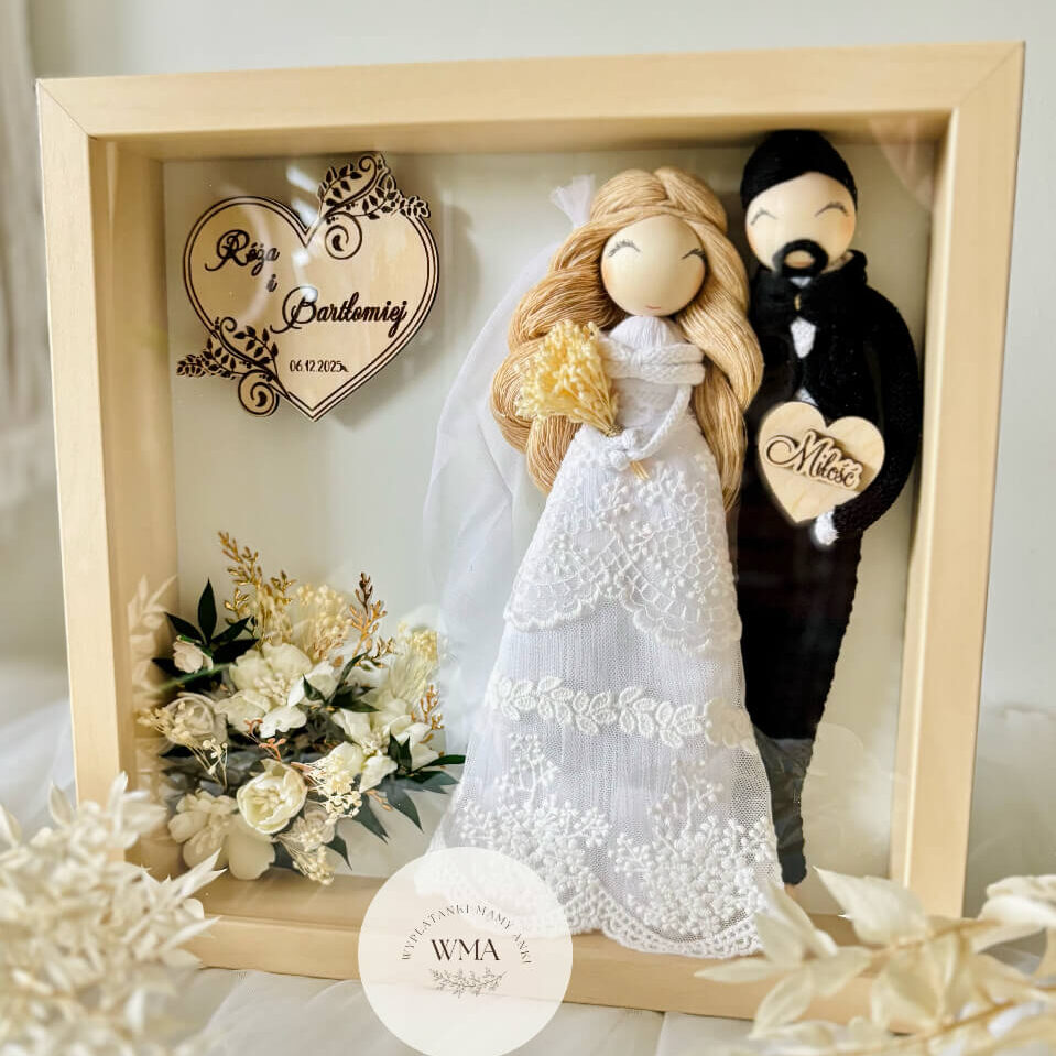Personalizowana ramka ślubna w naturalnej drewnianej ramie z figurkami pary młodej - panna młoda z długimi blond włosami w welonie i sukni koronkowej, pan młody z brodą w czarnym stroju z makramy, drewniane serce z imionami i datą ślubu, dekoracja z białych i kremowych kwiatów, serce z napisem Miłość, handmade