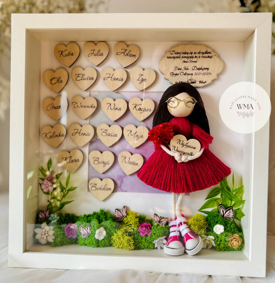 Personalizowana drewniana ramka z podziękowaniem dla nauczyciela z ręcznie robianą laleczką z długimi czarnymi włosami w bordowej sukience z frędzlami i złotymi okularami trzymającą serduszko Najlepsza Nauczycielka, drewniane serduszka z imionami uczniów, dekoracja z zielonego mchu, kwiatów i motyli, wyjątkowy prezent na Dzień Nauczyciela