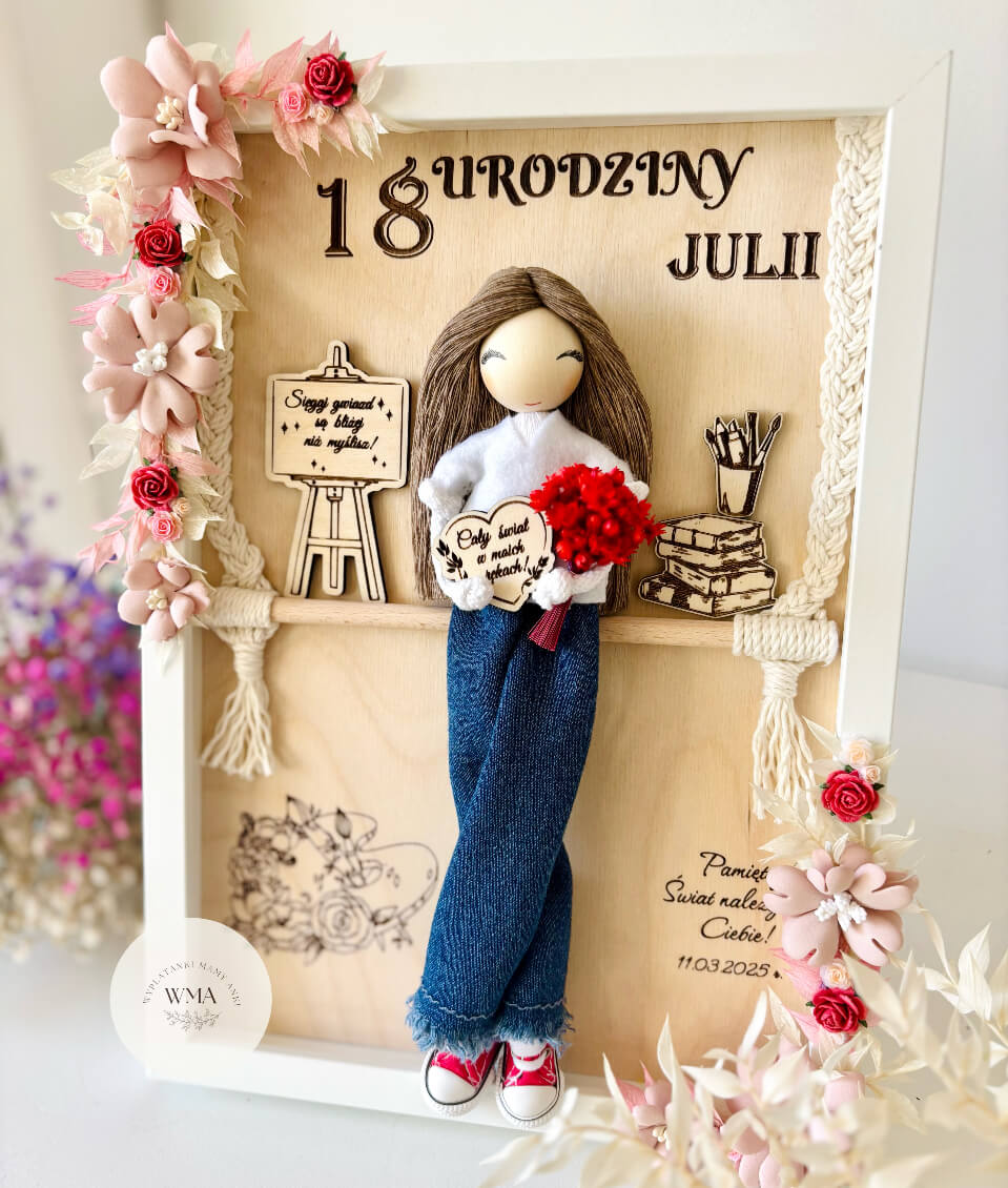 Personalizowana drewniana ramka na osiemnastkę z ręcznie robioną laleczką z brązowymi włosami w dżinsach trzymającą czerwony bukiet, drewniane elementy ze sztalugą i książkami, rama ozdobiona splotem makramy i różowo-czerwonymi kwiatami, wyjątkowy prezent