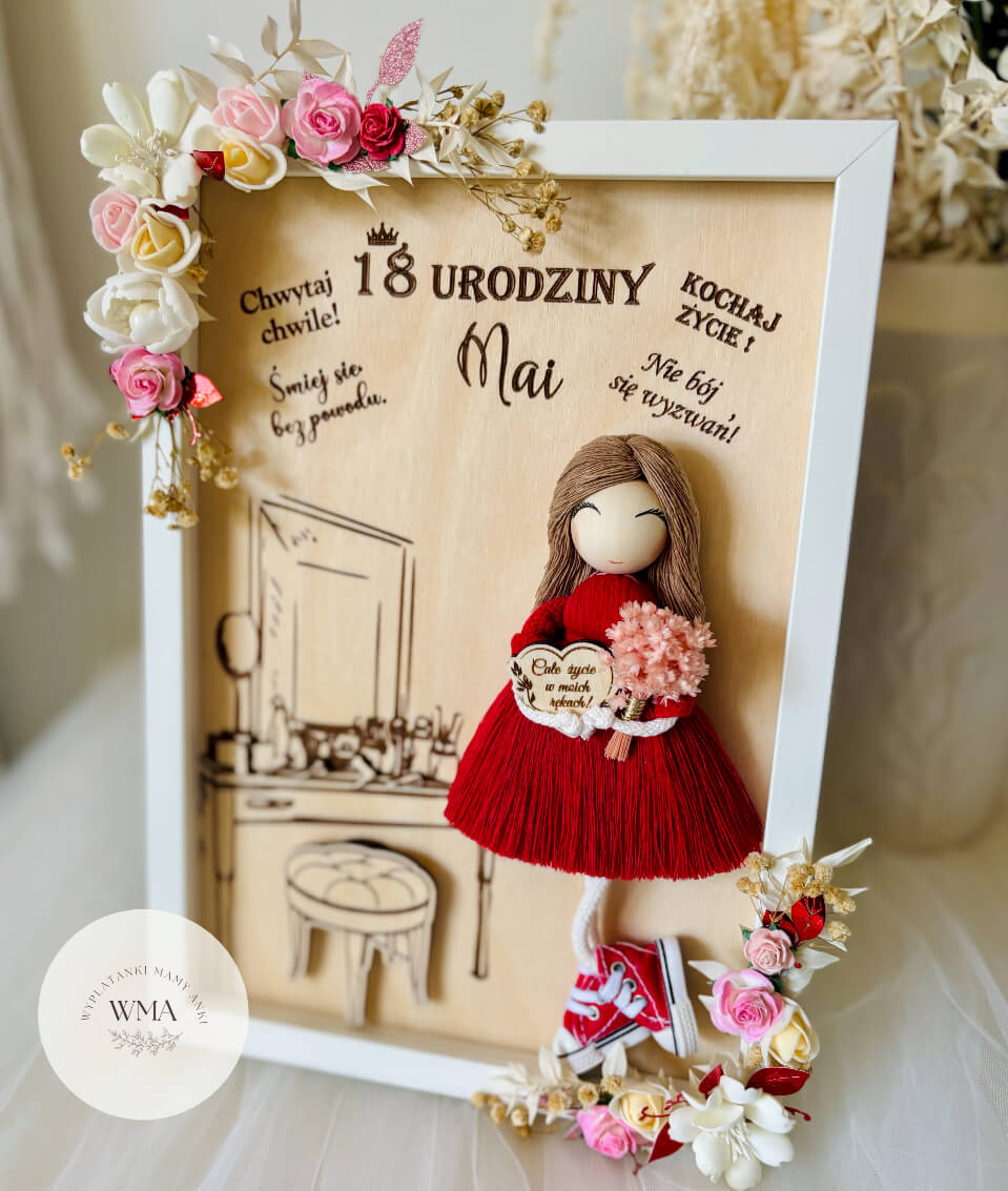 Personalizowana drewniana ramka na osiemnastkę z ręcznie robioną laleczką w czerwonej sukience z frędzlami trzymającą różowy bukiet, grawerowany motyw toaletki w tle, drewniane inskrypcje z życzeniami, biało-czerwona dekoracja kwiatowa, oryginalny prezent dla dziewczyny