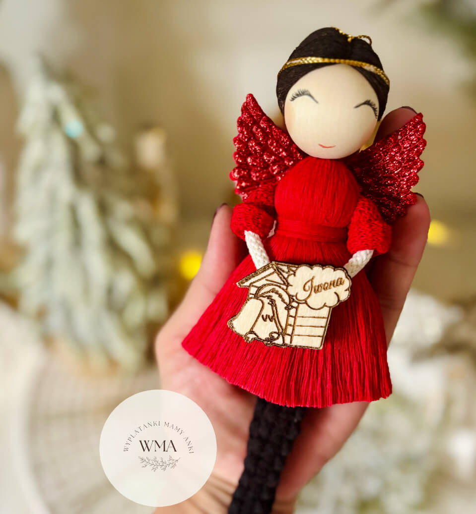 Czerwony aniołek z makramy z ciemnymi włosami i brokatowymi skrzydłami, trzymający personalizowaną zawieszką z pieskiem i imieniem – handmade prezent WMA