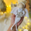 aniolek-swiateczny-bialy-makrame-skrzydla-sniezyna-zawieszka-choinkowa Aniołek świąteczny zawieszka w białym stroju makramé z tiulowymi skrzydłami i srebrną śnieżynką na tle świątecznych lampek WMA