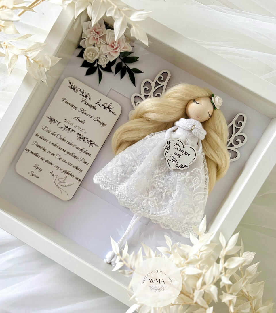 Pamiątka Pierwszej Komunii Świętej Amelii – aniołek z długimi blond włosami w białej koronkowej sukience z tabliczką z życzeniami